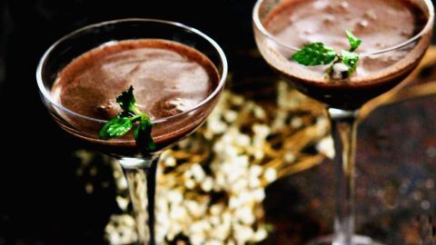 Zwei elegante Gläser mit Pfefferminz-Schoko-Drink stehen auf einer rustikalen Oberfläche, dekoriert mit grüner Minze.