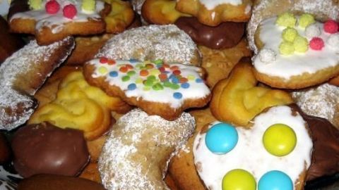 Vanillekipferl und bunte Kekse liegen auf einem Teller. Einige sind mit Zuckerguss und Schokoladenüberzügen verziert.