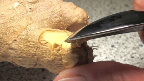 Ein handgehaltener Edelstahl-Teelöffel schält frischen Ingwer auf einer hellen Arbeitsplatte.
