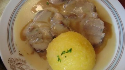 Sauerbraten-Scheiben mit Soße und Kartoffelknödel auf einem Teller, dekoriert mit etwas Petersilie, im Restaurant serviert.