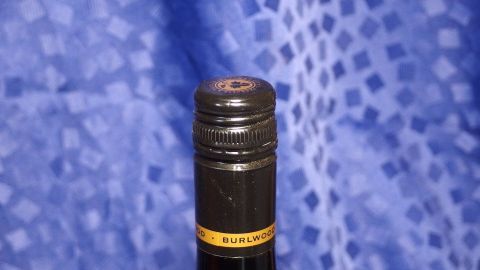 Eine Flasche Wein mit schwarzem Korken steht vor einem blauen, gemusterten Hintergrund, bereit zum Öffnen.