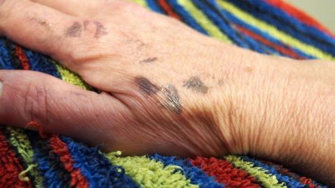 Eine Hand mit Farbflecken liegt auf einem bunten Handtuch und zeigt die Auswirkungen von Haartönung auf der Haut.
