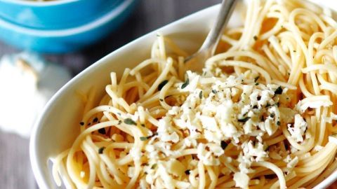 Eine Schüssel Knoblauch-Spaghetti liegt auf einem Tisch, während ein Löffel die pasta in der Schüssel umrührt.