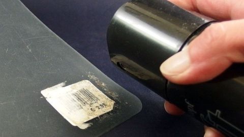 Eine Hand hält eine Haarspray-Dose, während sie Stickerreste von einer glatten Fläche entfernt.
