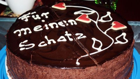 Ein runder Schokoladenkuchen liegt auf einem blauen Teller, dekoriert mit Herzen und der Schrift "Für meinen Schatz".