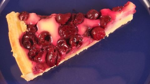 Ein Stück Creme fraiche-Kirschkuchen liegt auf einem blauen Teller und zeigt die saftigen Kirschen auf einer cremigen Schicht.