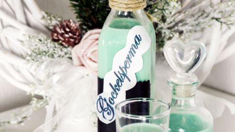 Eine Flasche mit grünlicher Flüssigkeit steht im Mittelpunkt, umgeben von Dekoration und einem Glas, das Gockelsperma etikettiert ist.