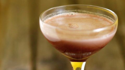 Ein elegantes Glas mit Pfefferminz-Schokoladentäfelchen-Likör steht auf einem rustikalen Holztisch, neben zwei Schokoladentäfelchen.