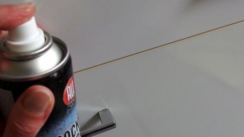 Mit Cockpitspray kann man kleine Kratzer in Kunststoff entfernen. Ein Handballen hält eine Spraydose mit Cockpitspray, während es auf eine Oberfläche mit kleinen Kratzern aufgetragen wird.