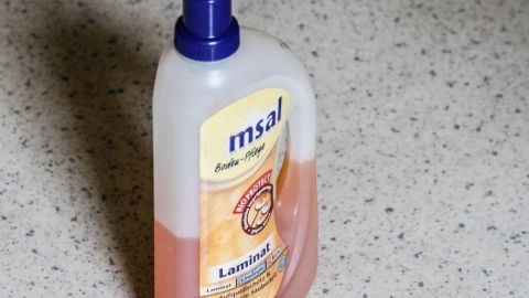 Mit ein paar Tropfen Möbelpolitur in deinem Wischwasser kannst du deinen PVC-Boden oder deinen Linoleum-Boden zum Glänzen bringen. (Abbildung ähnlich) Farbloser Möbelpoliturflasche steht auf einem PVC-Boden und wird verwendet, um den Glanz zu verbessern.