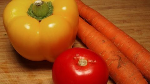 Buntes Ofengemüse besteht aus einer gelben Paprika, einer roten Tomate und zwei Karotten, die auf einem Holzbrett liegen.