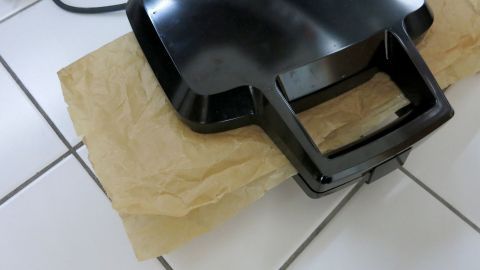 So vermeidet ihr die nervige Reinigung des Sandwichmakers: Packt eure Sandwiches einfach zwischen Backpapier! Ein Sandwichmaker liegt auf einem Stück Backpapier auf einem Fliesenboden, während er darauf wartet, benutzt zu werden.