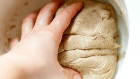 Ein Hand greift in einen Teig, während er in einer Schüssel geknetet wird, um Hefeteig ohne Kleben zu formen.