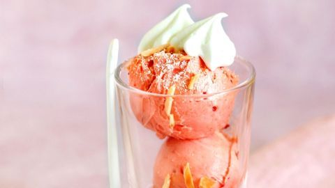 Schälchen mit Low-Carb-Fruchteis, dekoriert mit Sahne und eine Erdbeere, auf einem rosa Tischcloth.