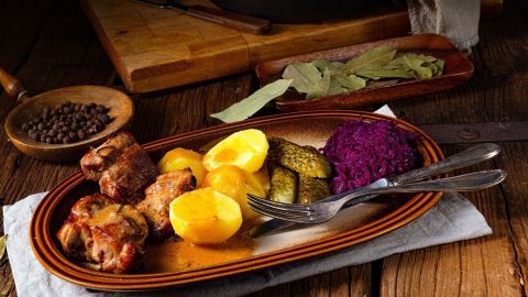 Ein Teller mit Ostfriesischem Snirtjebraten zeigt saftiges Fleisch, Kartoffeln, rote Beete und Gewürzgurken, garniert auf einem rustikalen Tisch.