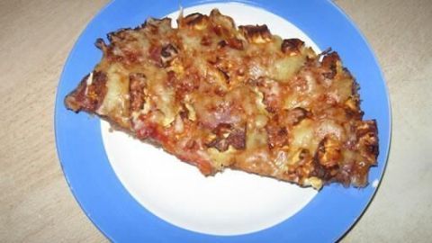 Eine Stück Hackfleischpizza ohne Teig liegt auf einem weißen Teller mit blauer Umrandung und zeigt eine goldbraune, belegte Oberfläche.