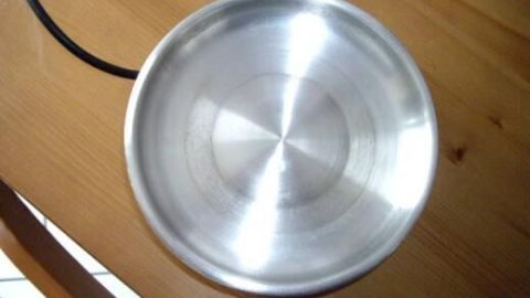 Ein metallener Eierkocher steht auf einem Holztisch; sein glänzender, sauberer Innenboden reflektiert das Licht.
