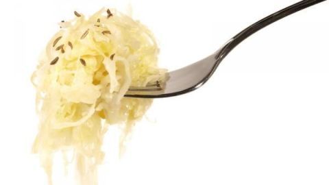 Ein Gabel mit Sauerkraut hält einen Haufen des fermentierten Gemüse. Der Hintergrund ist neutral und hell.
