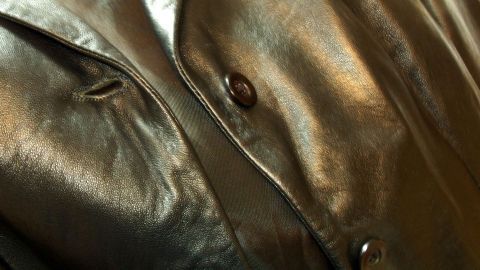 Eine glänzende Lederjacke liegt locker mit einem Knopf offen, umgeben von sanftem Licht, das die Struktur des Leders betont.