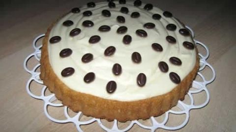 Eine Vanille-Quark-Torte ohne Backen liegt auf einem weißen Tortengitter, dekoriert mit Kaffeebohnen auf einer cremigen Oberfläche.
