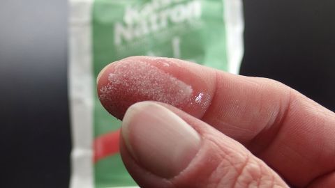 Ein Finger hält ein wenig Kaiser Natron Pulver, während eine Packung im Hintergrund sichtbar ist.