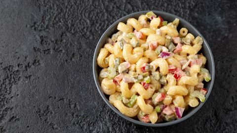 Ein pastellfarbenes Nudelsalatgericht mit kleinen Teigwaren, gemischtem Gemüse und Fleischstücken in einer cremigen Sauce.