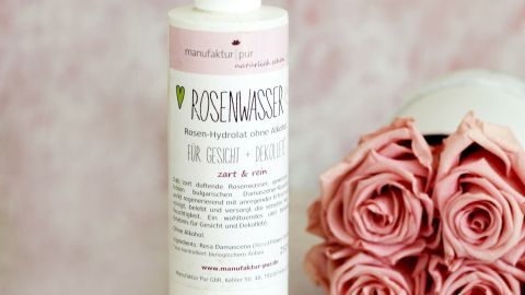 Eine Flasche Rosenwasser sprüht sanft in der Nähe von frischen, zarten Rosen. Die Umgebung ist hell und harmonisch.