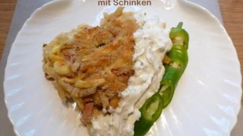 Ein Stück Nudelauflauf mit Schinken liegt auf einem Teller neben türkischem Knoblauch-Joghurt und grüner Paprika. Text: "Herzhafter Nudelauflauf mit Schinken und türkischer Knoblauch-Yoghurt".