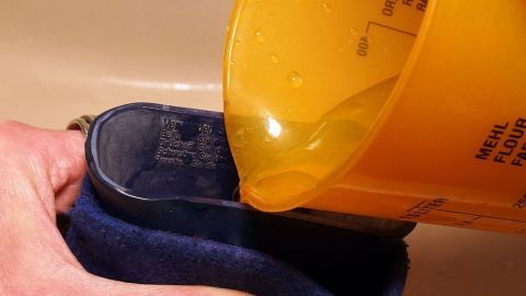 Eine Person füllt eine Wärmflasche mit heißem Wasser aus einem gelben Behälter, um sie warm zu halten.