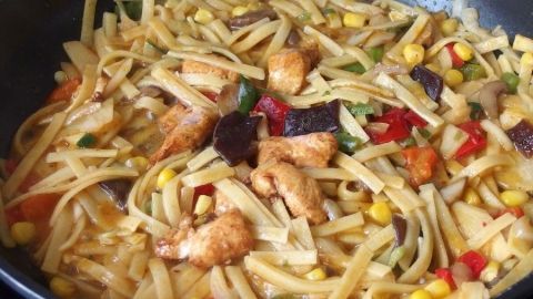 Gebratene Nudeln werden in einer Pfanne zubereitet, vermischt mit buntem Gemüse und Fleischstücken, aromatisch und appetitlich.