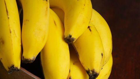 Gelbe Bananen liegen in einer braunen Schale auf einem gestreiften Tuch, bereit für den Einsatz gegen Warzen.