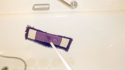 Ein Wischmop liegt in einer Badewanne, während er gleichzeitig zum Reinigen verwendet wird, was Rückenschmerzen vermeidet.