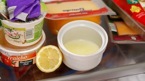 Ein Behälter mit einer gelben Flüssigkeit steht neben einer halbierten Zitrone im Kühlschrank, um unangenehme Gerüche zu neutralisieren.