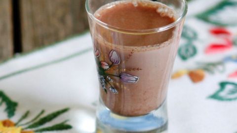 Ein dekoratives Glas mit einer braunen Flüssigkeit steht auf einem blumengemusterten Tischläufer aus Stoff.