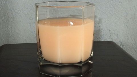 Ein Glas Wodka mit Krümeltee steht auf einem dunklen Tisch, umgeben von einer schlichten Wand, leicht trüb und beige.