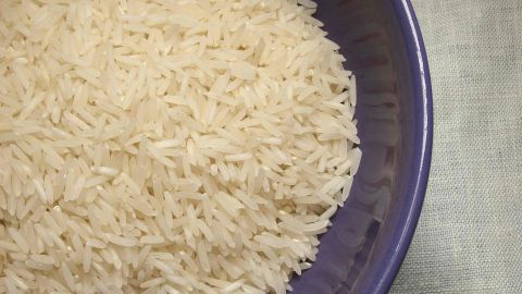 Körner Reis in einer lila Schüssel, angeordnet auf einem hellen, strukturierten Untergrund, bereit zum Kochen.