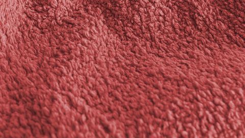 Wenn Handtücher mit Weichspüler gewaschen werden, verlieren sie an Saugkraft und fusseln. Rote Handtücher liegen auf einer Oberfläche, ihre leicht fusselige Struktur deutet auf Weichspüler-Anwendung hin.