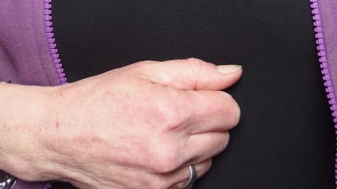 Eine Hand ist zu einer Faust geballt und drückt gegen die Bauchgegend, um Sodbrennen wegzuklopfen.