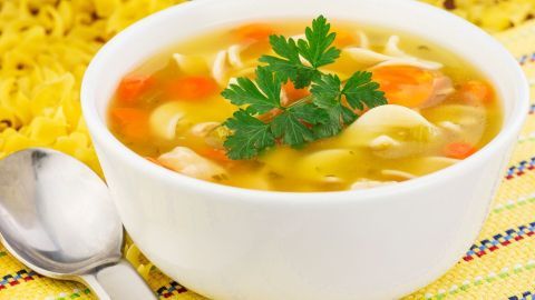 Eine weiße Schüssel mit Hähnchensuppe steht auf einem bunten Tuch, garniert mit frischer Petersilie.