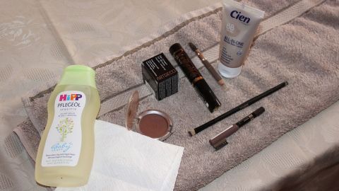 Auf einem Handtuch liegen verschiedene Kosmetikprodukte, darunter Babyöl, Feuchtigkeitscreme und Make-up.