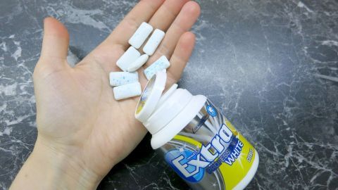 Eine Hand hält Kaugummi-Stücke, während eine geöffnete Dose auf einer dunklen Oberfläche steht, die zur Linderung von Sodbrennen genutzt werden kann.