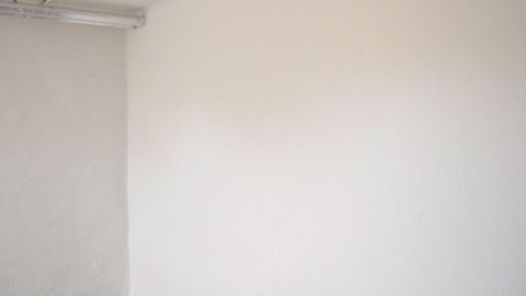 Eine weiße Wand mit leichten Klebebandresten zeigt den Bereich, wo zuvor etwas haftete, in einem neutralen Raum.