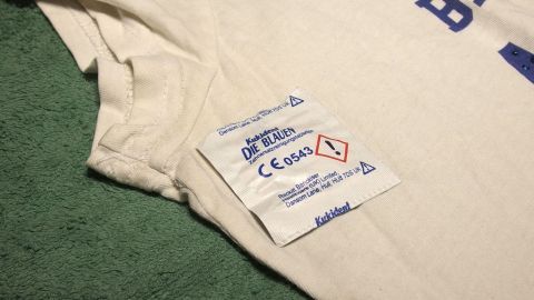 Ein T-Shirt liegt auf einem grünen Tuch, das Pflegeetikett zeigt Anweisungen zur Reinigung und Pflege.