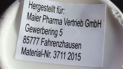 Mit kosmetischem Haarwasser lassen sich Aufkleber von Glas und Porzellan, sowie von Töpfen, ganz leicht entfernen. Ein Etikett auf einem Behälter zeigt Informationen über das kosmetische Haarwasser und dessen Hersteller an.