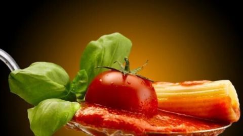 Ein Löffel mit Tomatensoße hält frisches Basilikum, eine Kirschtomate und Rigatoni in leuchtendem Licht.
