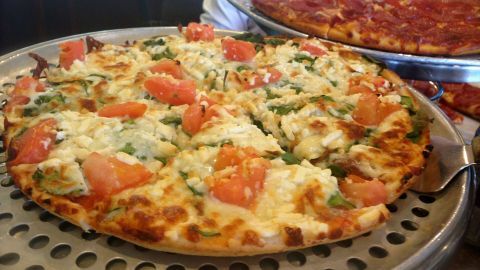 Eine frisch gebackene Pizza, belegt mit Tomaten und Gemüse, liegt auf einem Servierblech in einer Pizzeria.