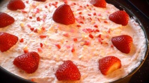 Eine Erdbeertorte, bedeckt mit Sahne und dekoriert mit ganzen Erdbeeren, liegt in einer Kuchenform auf einem Tisch.