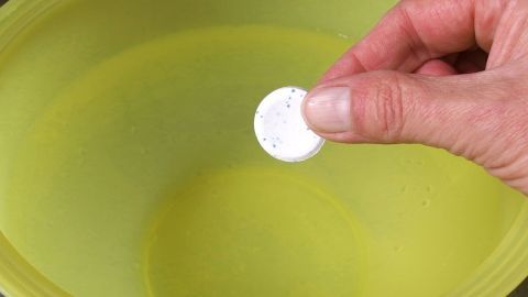 Eine Hand hält einen Gebissreiniger über eine gelbe Schüssel mit Wasser.