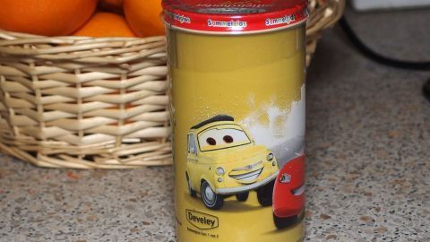 Ein Senfglas mit einem bunten Autos-Motiv steht auf einer Küchentheke, umgeben von einer Obstschale.