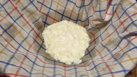 Ein frischer Quark liegt auf einem karierten Küchentuch, das zum Abtropfen verwendet wird. Die Umgebung ist heimisch und einladend.